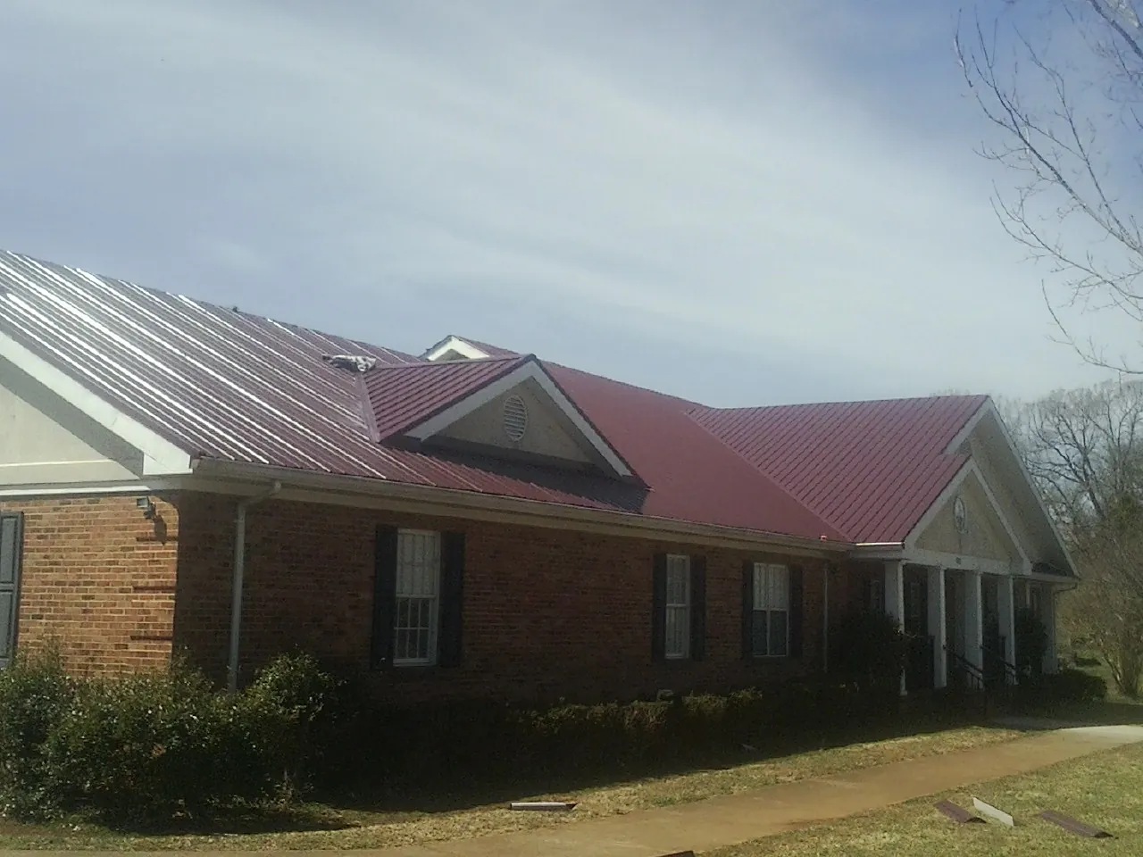 Red metal roof with gabled entries on a long brick building, from a Hail Damage Roof Repair job in Royston