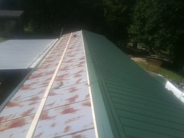 Old rusted panels beside newly installed green metal roofing — Wind Damage Roof Repair by Roofing Brothers in Royston