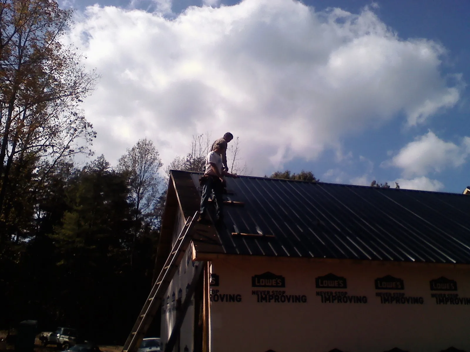 Roofer fastening dark metal panels high against a cloudy sky, from a Roof Inspection job in Royston