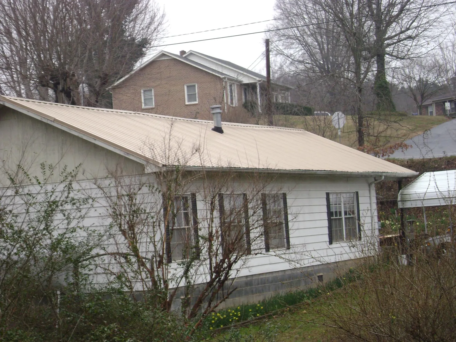 Tan metal roof on a white sided house set into a hillside — Commercial Roofing by Roofing Brothers in Royston